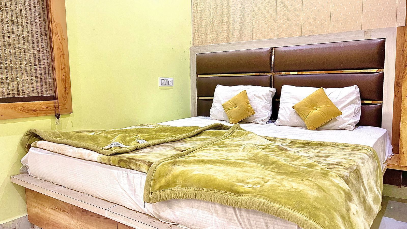 A bed with a green blanket and two pillows, a wooden headboard, and a wall socket.