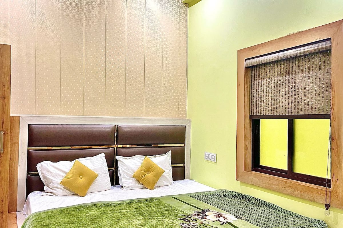 A bedroom with a bed, a window with blinds, and a wall-mounted air conditioning unit.
