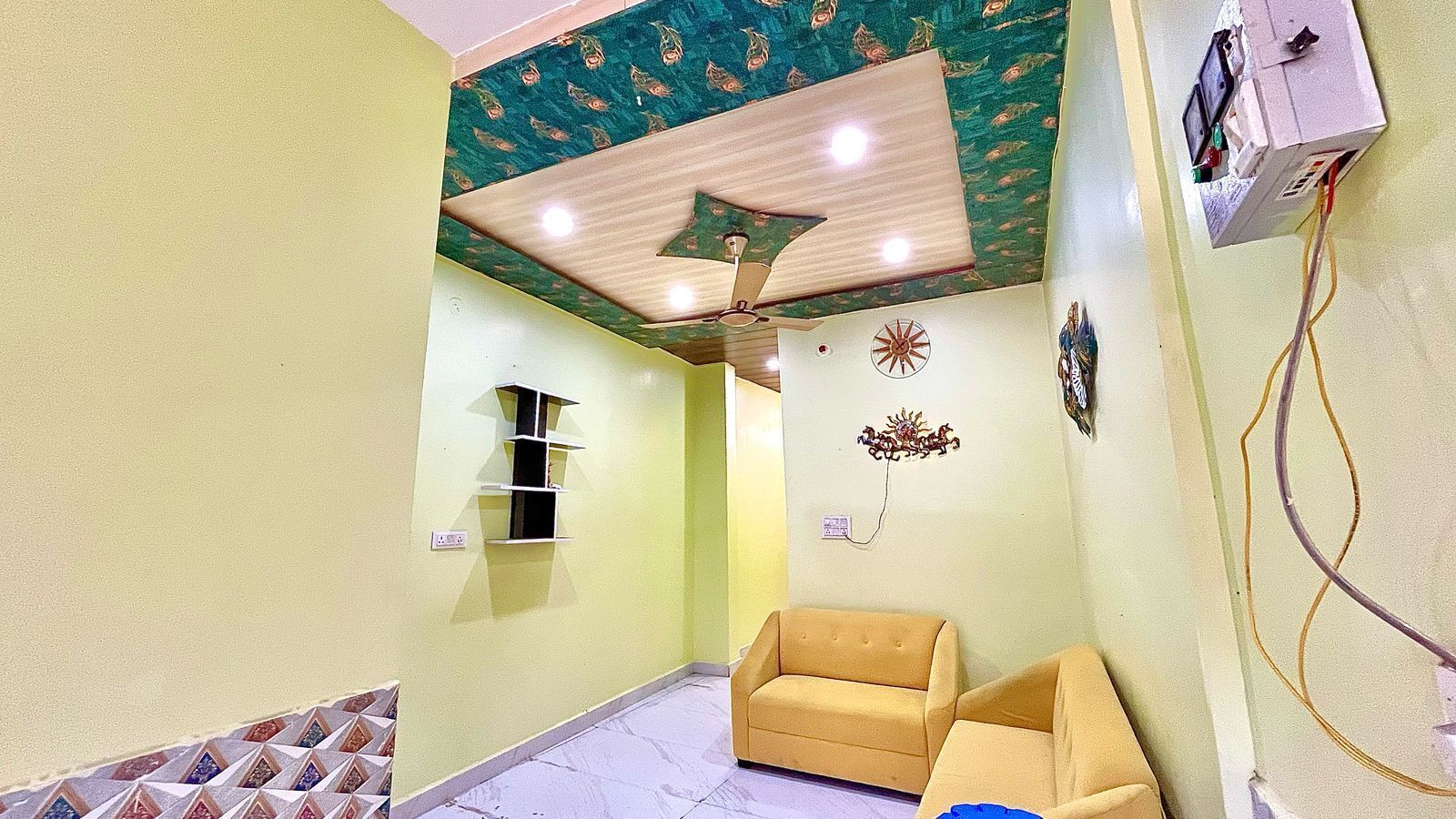 A room with a ceiling fan, a wall-mounted electrical box, and a sofa.