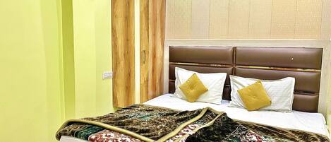 A bed with a patterned blanket, a wooden wardrobe, and a headboard with two pillows.