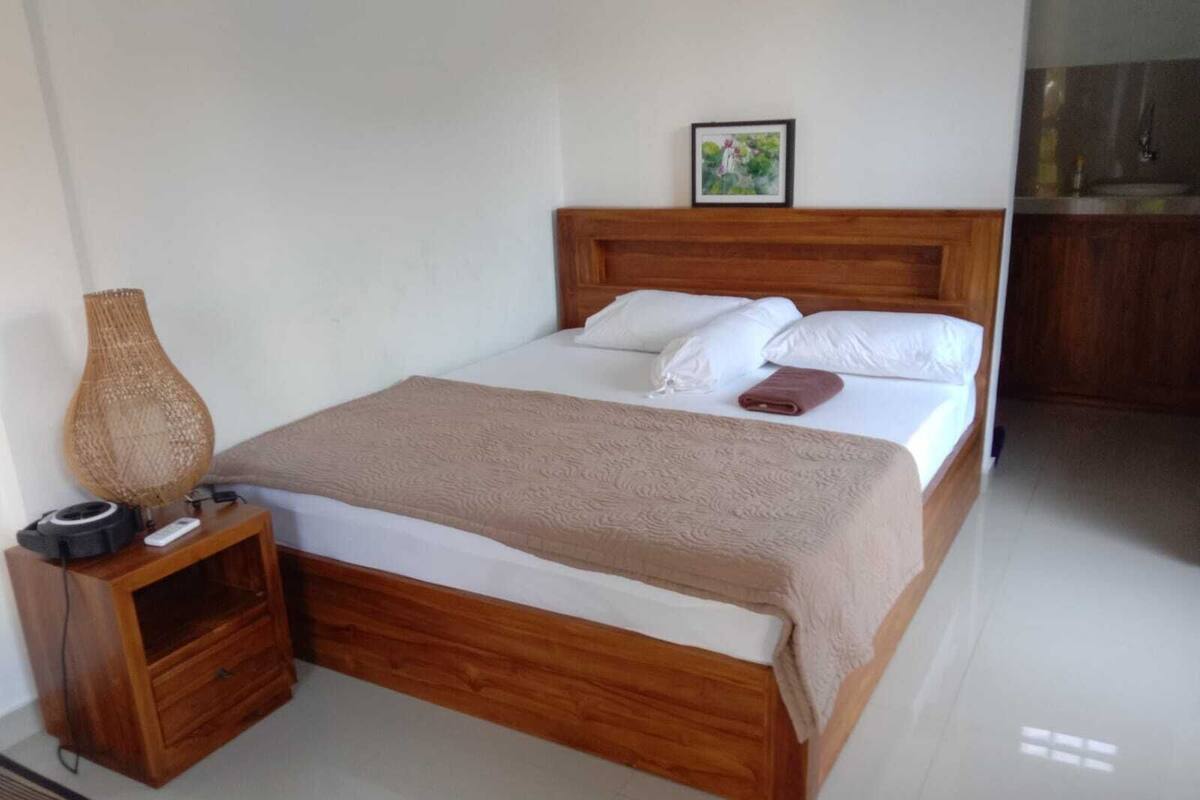 A neatly made bed with a wooden headboard, a bedside table with a lamp, and a framed picture on the wall.