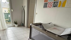 Habitació amb bressol, planta en test i paret amb obra d'art colorida.