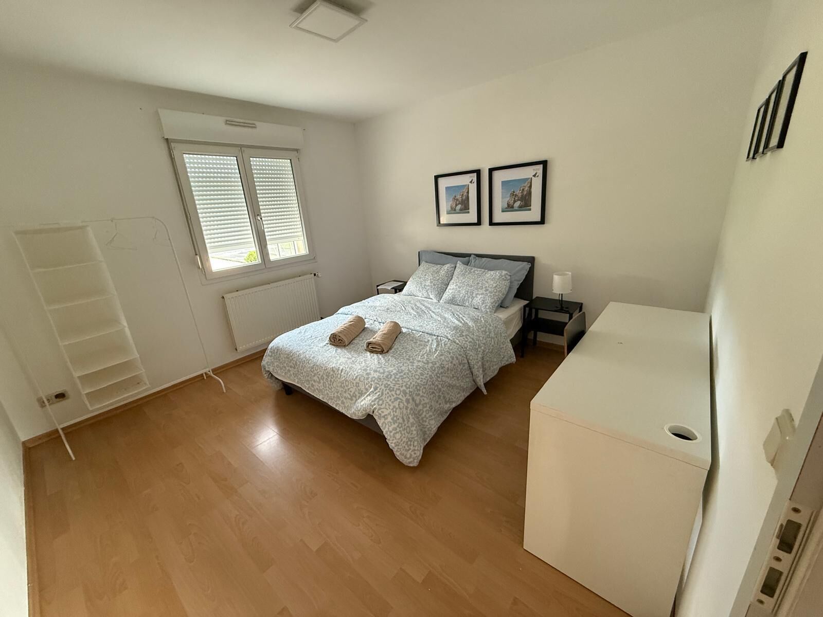 Un dormitorio con cama, mesitas de noche, radiador, ventana con persianas y un armario blanco.