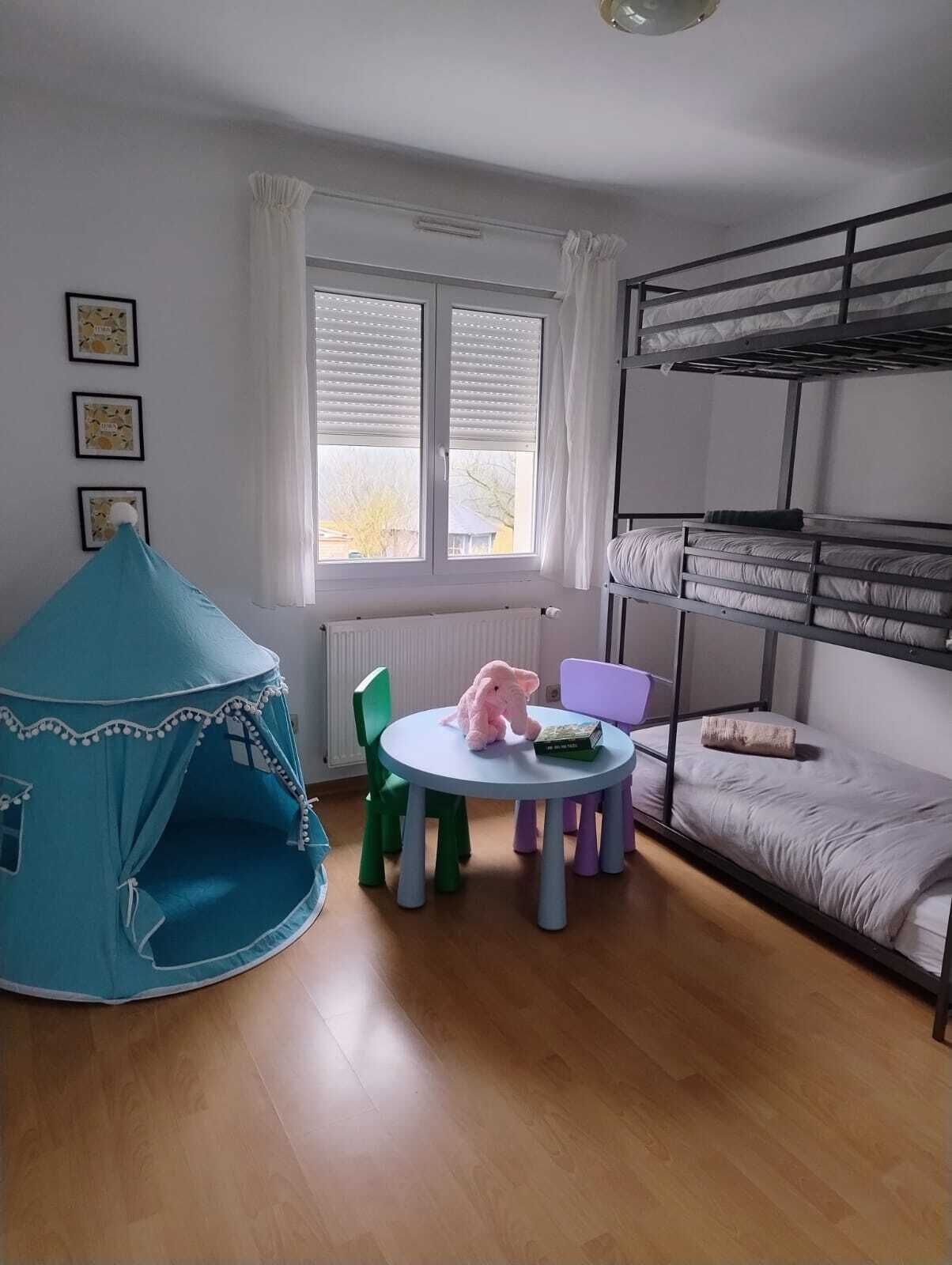 Une pièce avec des lits superposés, une tente, une table avec des chaises et un jouet en peluche.