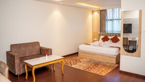 A modern hotel room with a sofa, a small table, a bed with pillows, a mirror, and a TV. - Hotel badrinath (Kathmandu)