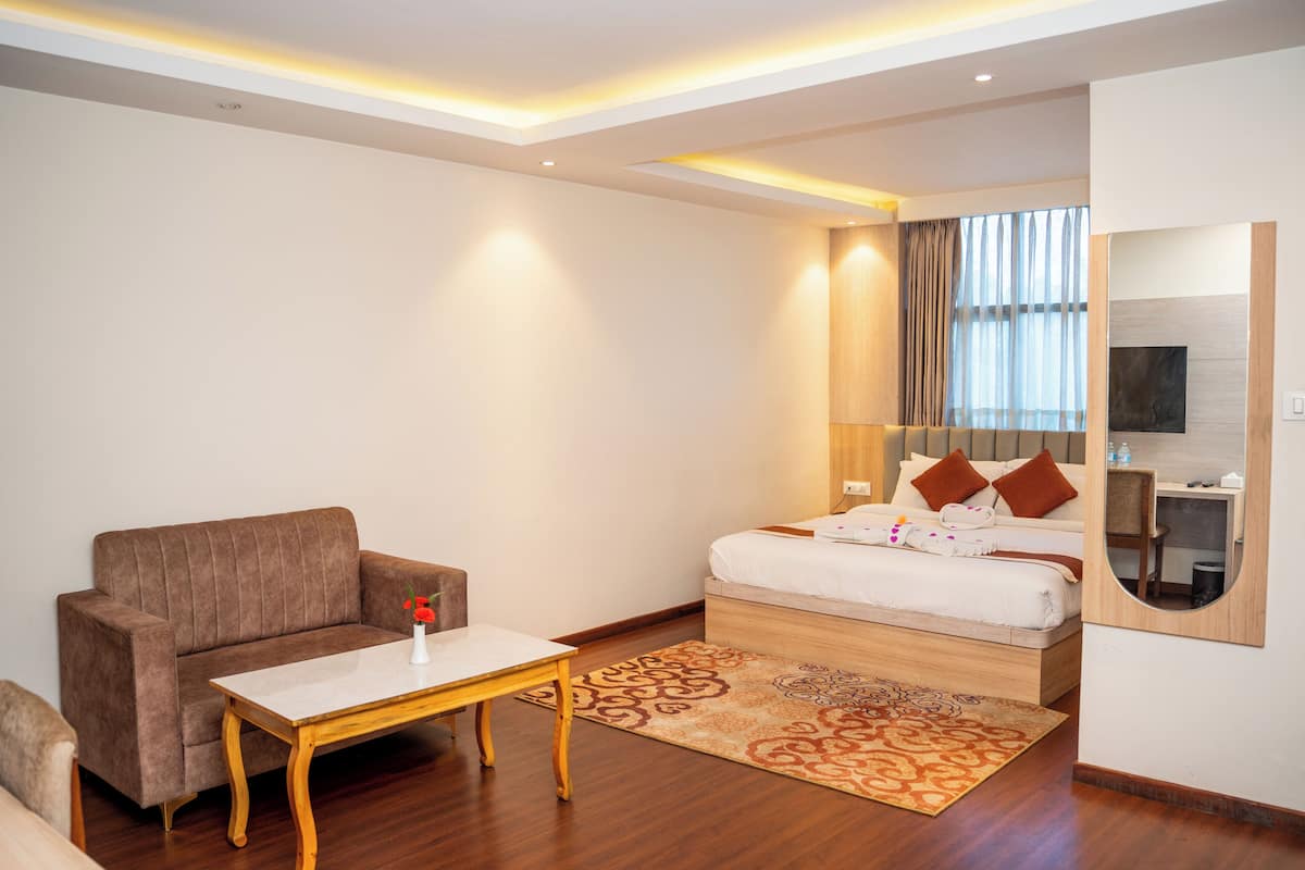 A modern hotel room with a sofa, a small table, a bed with pillows, a mirror, and a TV.