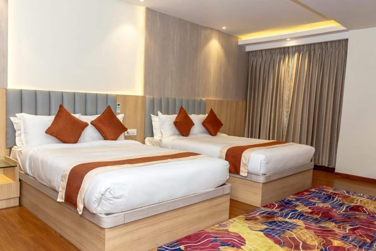 A hotel room with two beds, a glass bedside table, a wooden nightstand, and a colorful rug.