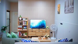 En moderne stue med et fladskærms-tv, en træbogreol og en ventilator.