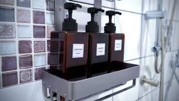 Un baño con pared de azulejos, ducha y repisa para dispensador de jabón con dos botellas que dicen "CONDITIONER" y "SHAMPOO".