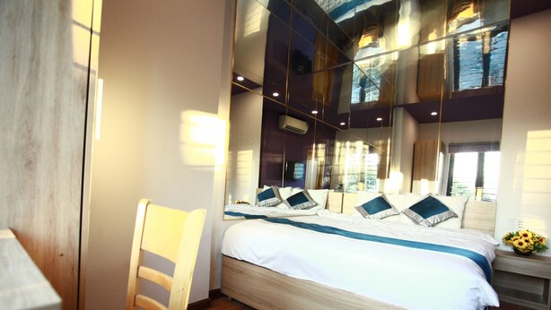 A modern hotel room with a large bed, wooden headboard, and a mirror reflecting the room's interior. - Mata Love hotel (Da Nang)