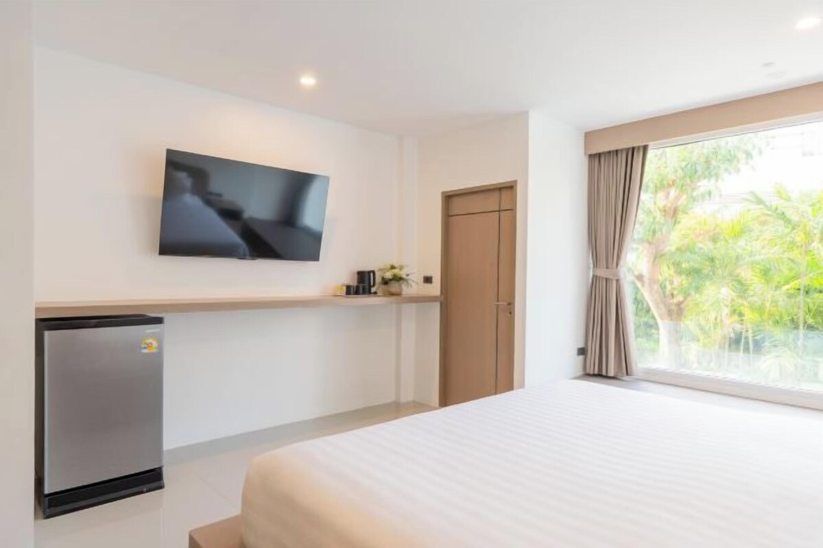 A hotel room with a bed, a television mounted on the wall, a minibar, and a window with curtains.