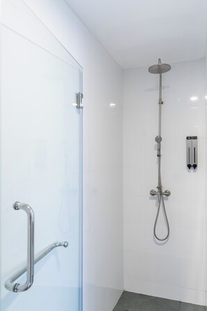A modern bathroom with a glass shower enclosure, a handheld showerhead, and a wall-mounted control panel. - Sunnyside Kata (Karon)