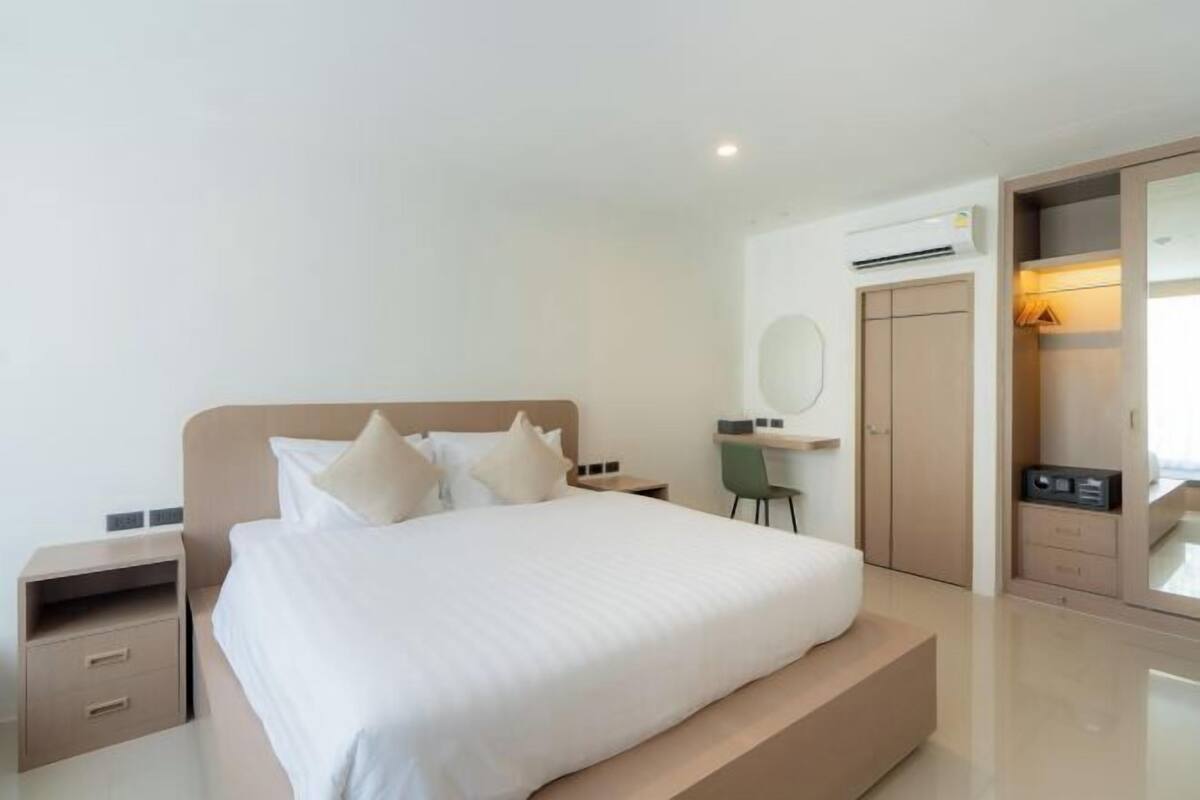 A modern hotel room with a large bed, a desk, a chair, and a wardrobe.