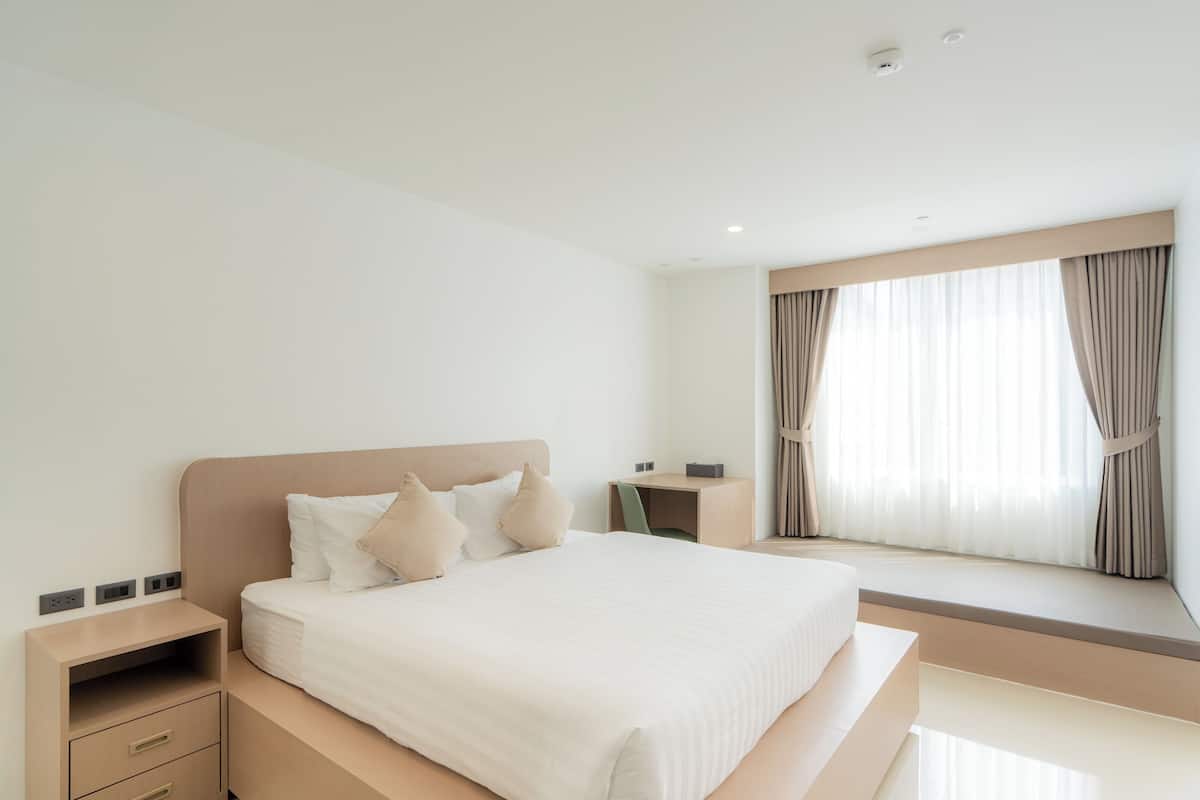 A modern hotel room with a large bed, bedside tables, a desk, and a window with curtains.