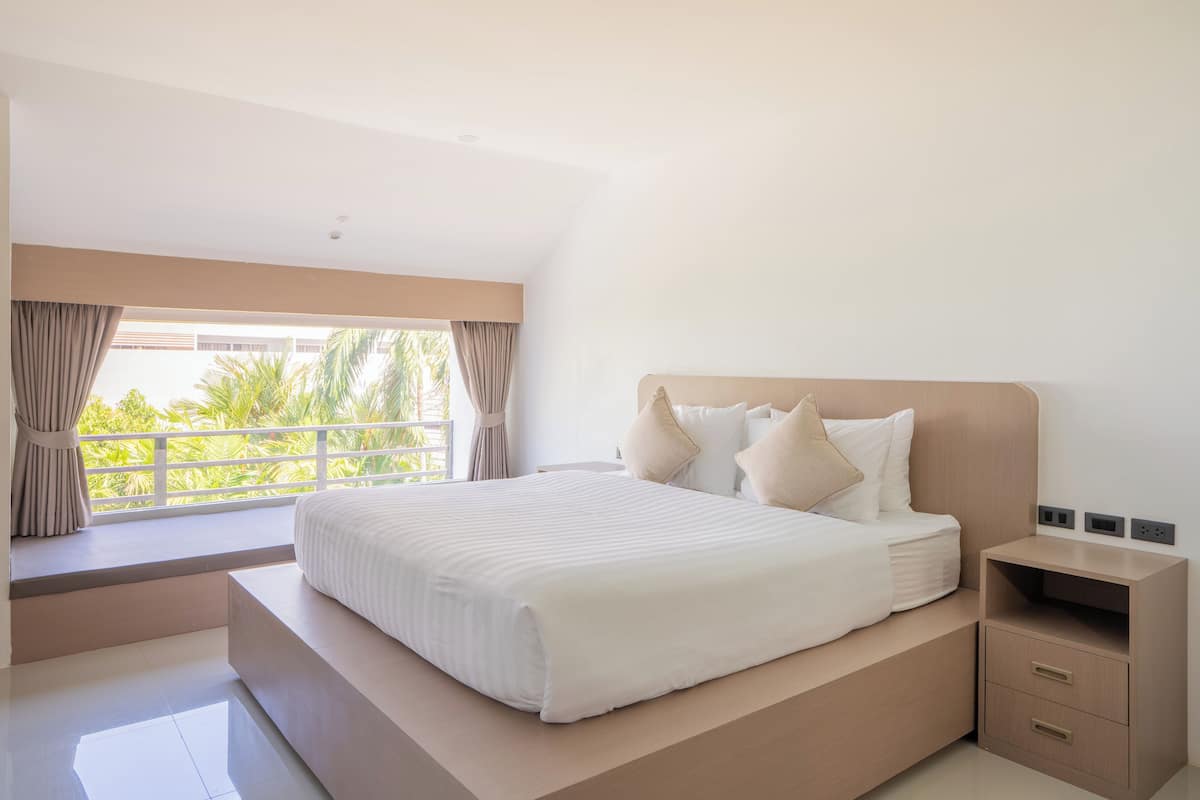 A modern bedroom with a large bed, a nightstand, and a window with curtains.