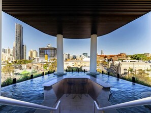 Une piscine à débordement offrant une vue sur le paysage urbain, soutenue par des colonnes, et deux tabourets de bar.