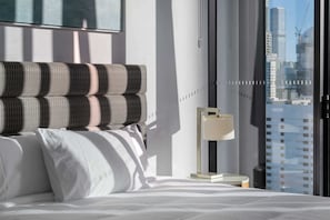 Une chambre d’hôtel moderne avec un grand lit, une table de chevet, une lampe et une vue sur le paysage urbain par la fenêtre.