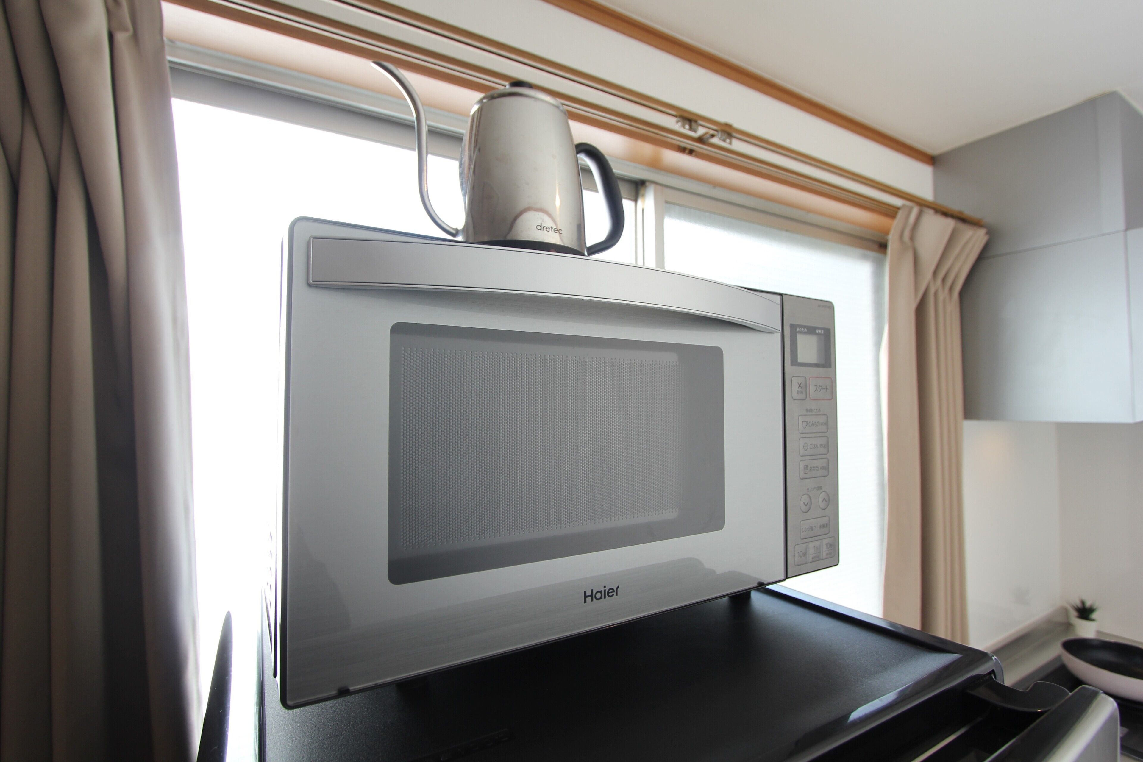 Uma cozinha moderna com micro-ondas Haier, chaleira e janela com cortinas.
