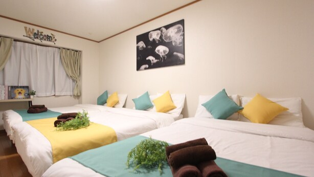 A hotel room with two beds, each with a different colored bedspread, pillows in various colors, and a welcome sign on the wall. - LUANA HOTELU NISHIKI (Tokyo)