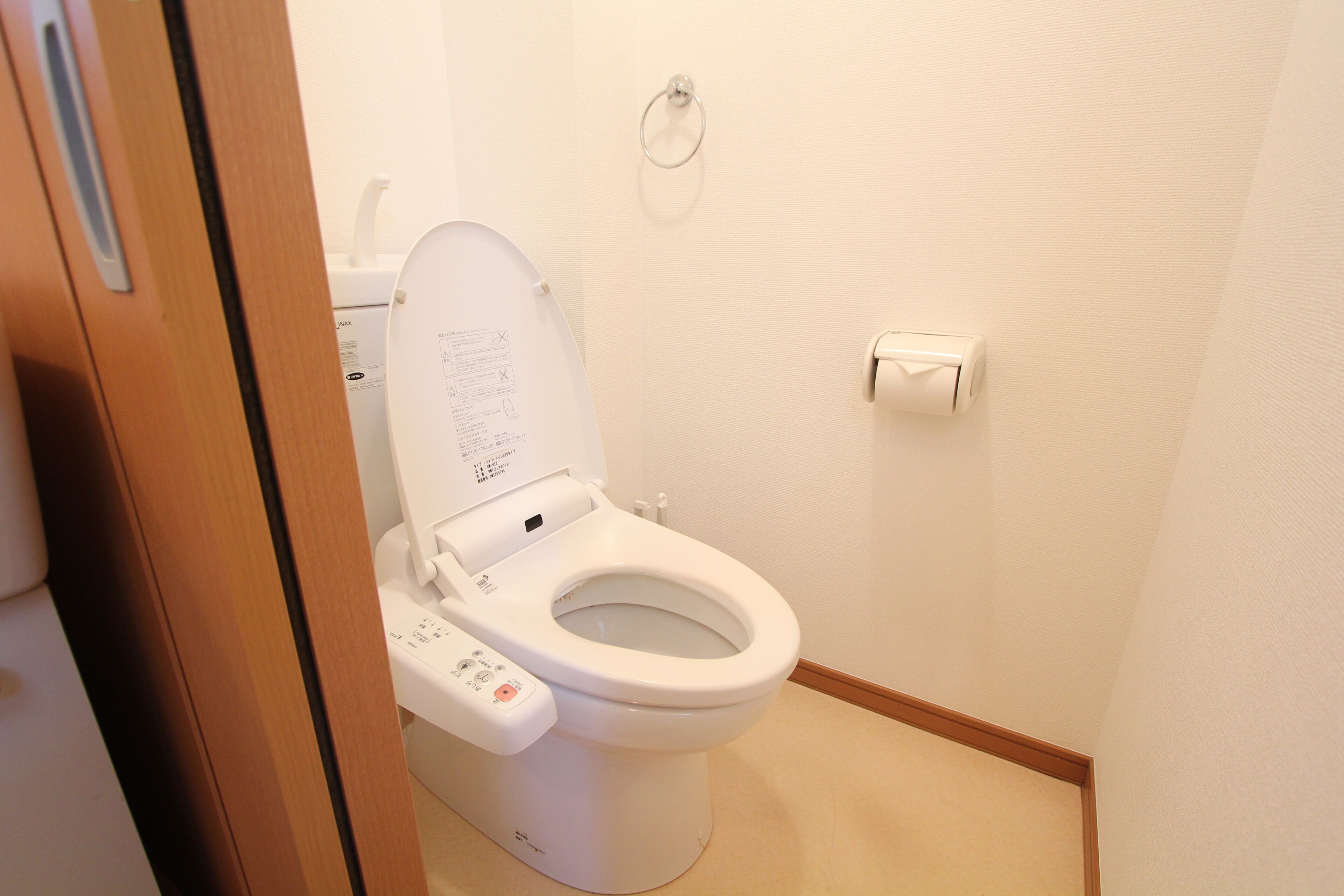 A white toilet with a control panel, a toilet paper holder on the wall, and a wooden door frame.