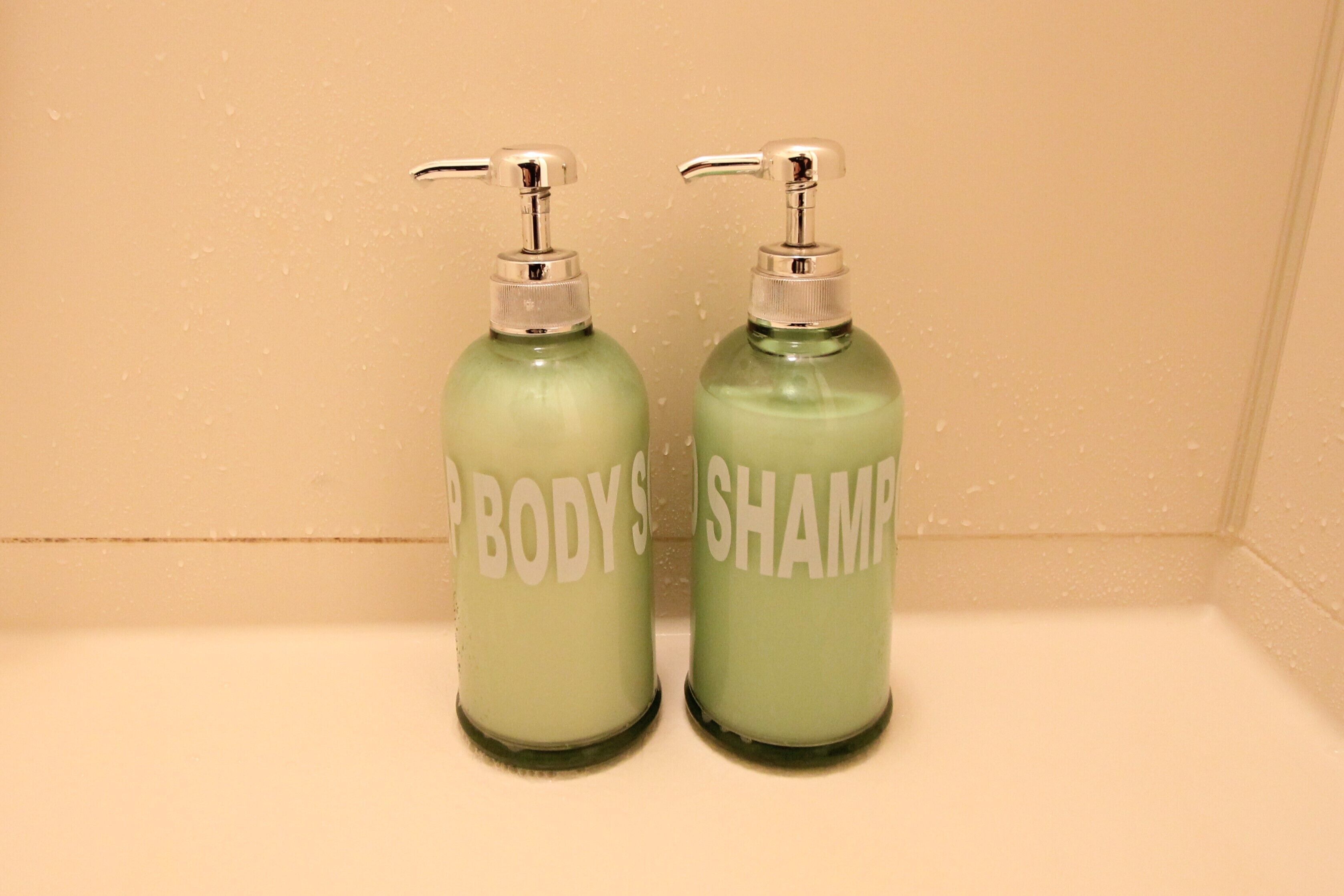 Two green bottles with pumps labeled "BODY" and "SHAMPOO" on a shelf.