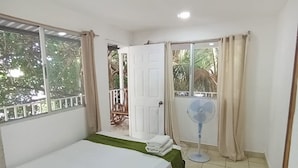 A bedroom with a bed, a fan, a door, and a view of the outside.