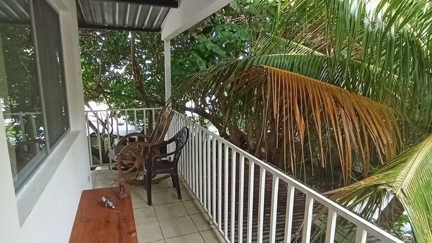 A balcony with a wooden table and chairs, surrounded by a white railing and lush greenery.