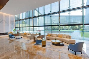 A spacious lobby with a large glass wall, a beige sofa set, and a blue armchair. - Shanghai International Tourist Resort Fuyi Hotel (Shanghai)