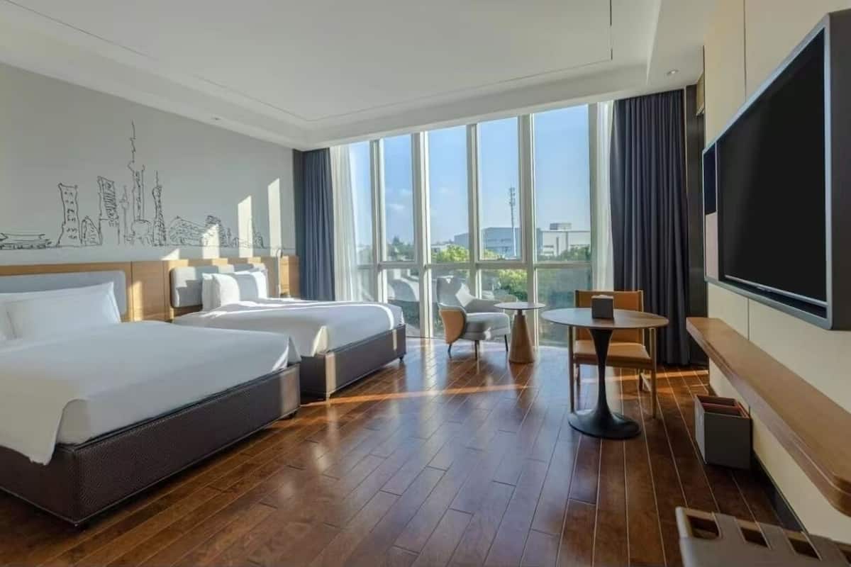 Ein Hotelzimmer mit zwei Betten, einem Balkon mit Aussicht, einem Fernseher und einem kleinen Tisch.
