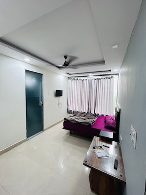 Ein Hotelzimmer mit Bett, Schreibtisch, Stuhl, Deckenventilator und einem Fenster mit Vorhängen.
