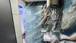 Un baño con pared de mármol, separador de vidrio, inodoro, lavamanos y zona de ducha.