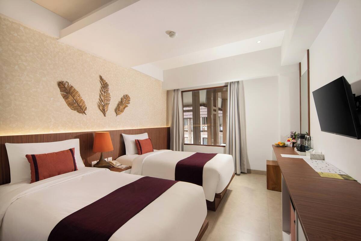 A hotel room with two beds, a desk, a TV, and a window with curtains.