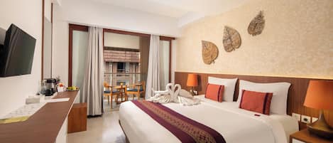 A hotel room with a bed, a desk, a TV, a dining area, and a wall with decorative leaves.