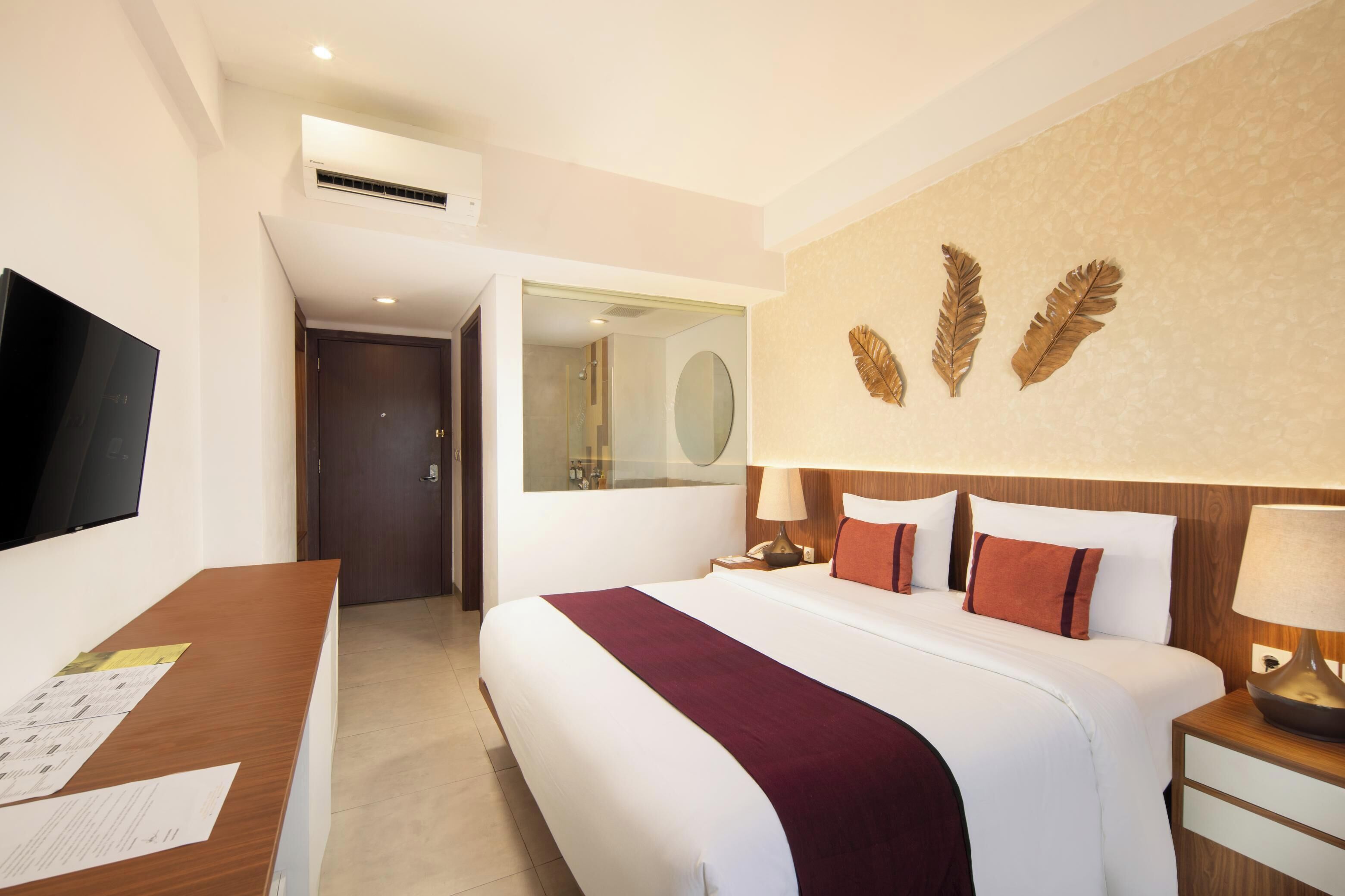 Une chambre d’hôtel avec un lit, un bureau avec des papiers, une télévision, un miroir et un mur décoré de motifs végétaux.