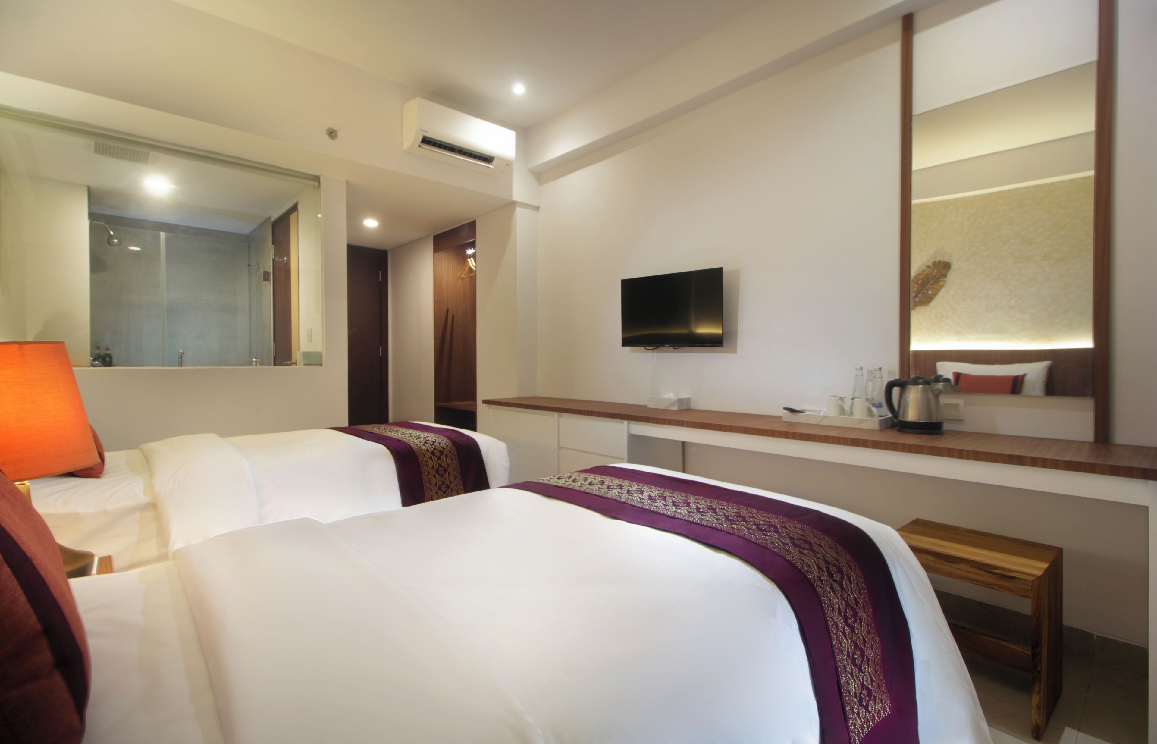 A hotel room with two beds, a desk, a TV, and a mirror.