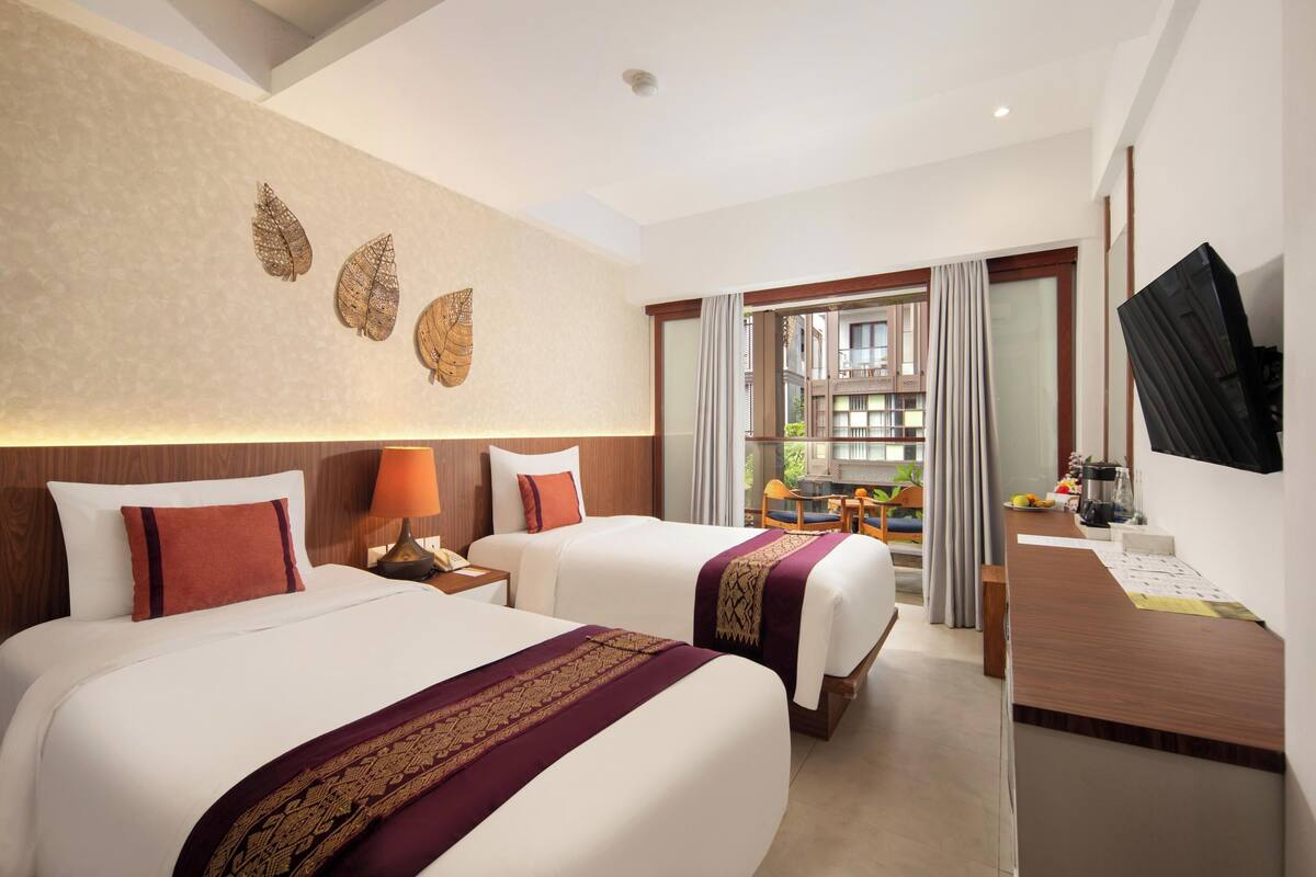 A hotel room with two beds, a desk, a TV, and a view of the outside.