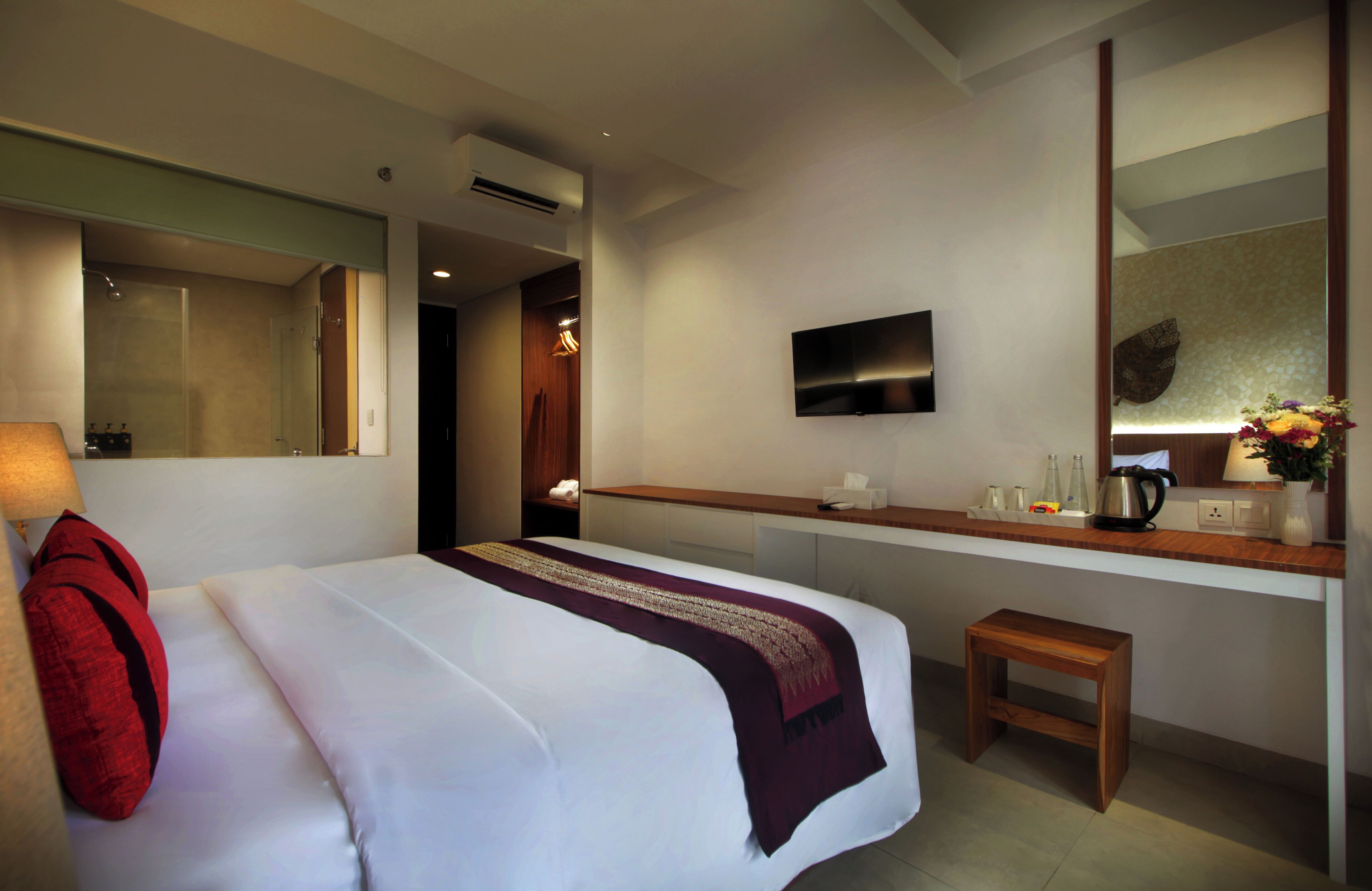A hotel room with a bed, a bedside table, a TV, a mirror, and a small wooden stool.