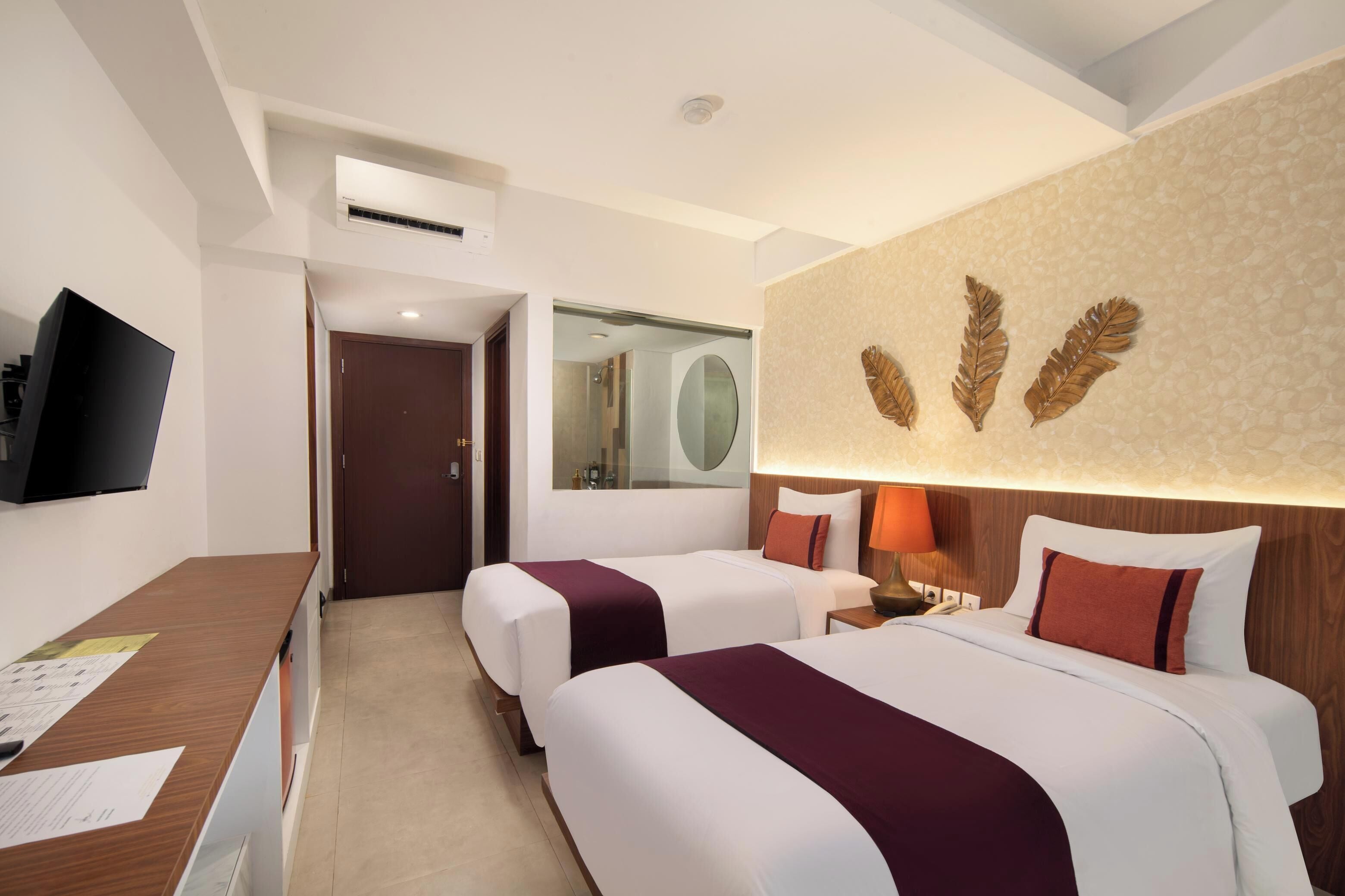 A hotel room with two beds, a desk, a television, and a mirror.