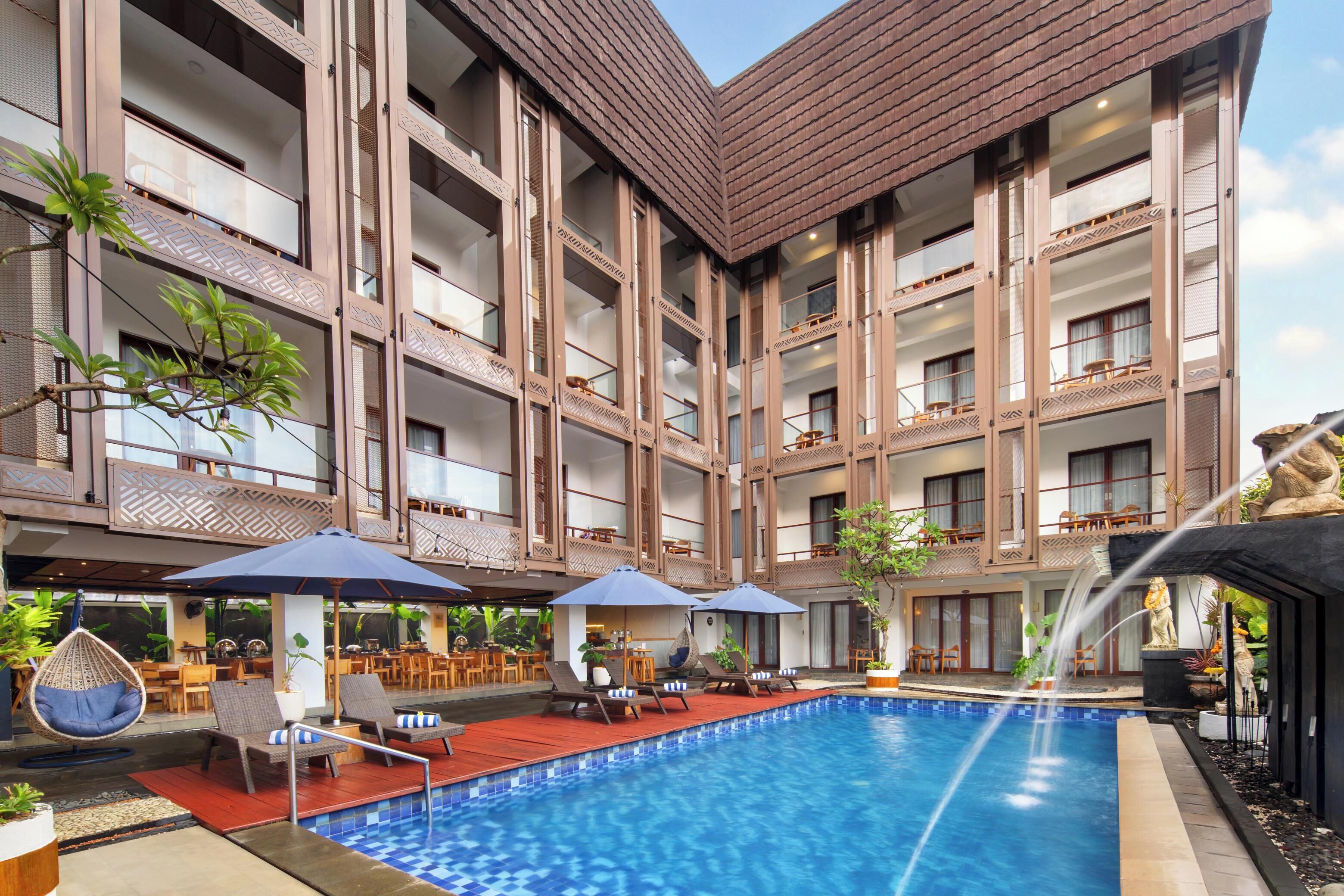 A hotel with a swimming pool, outdoor seating, and a multi-story building with balconies.