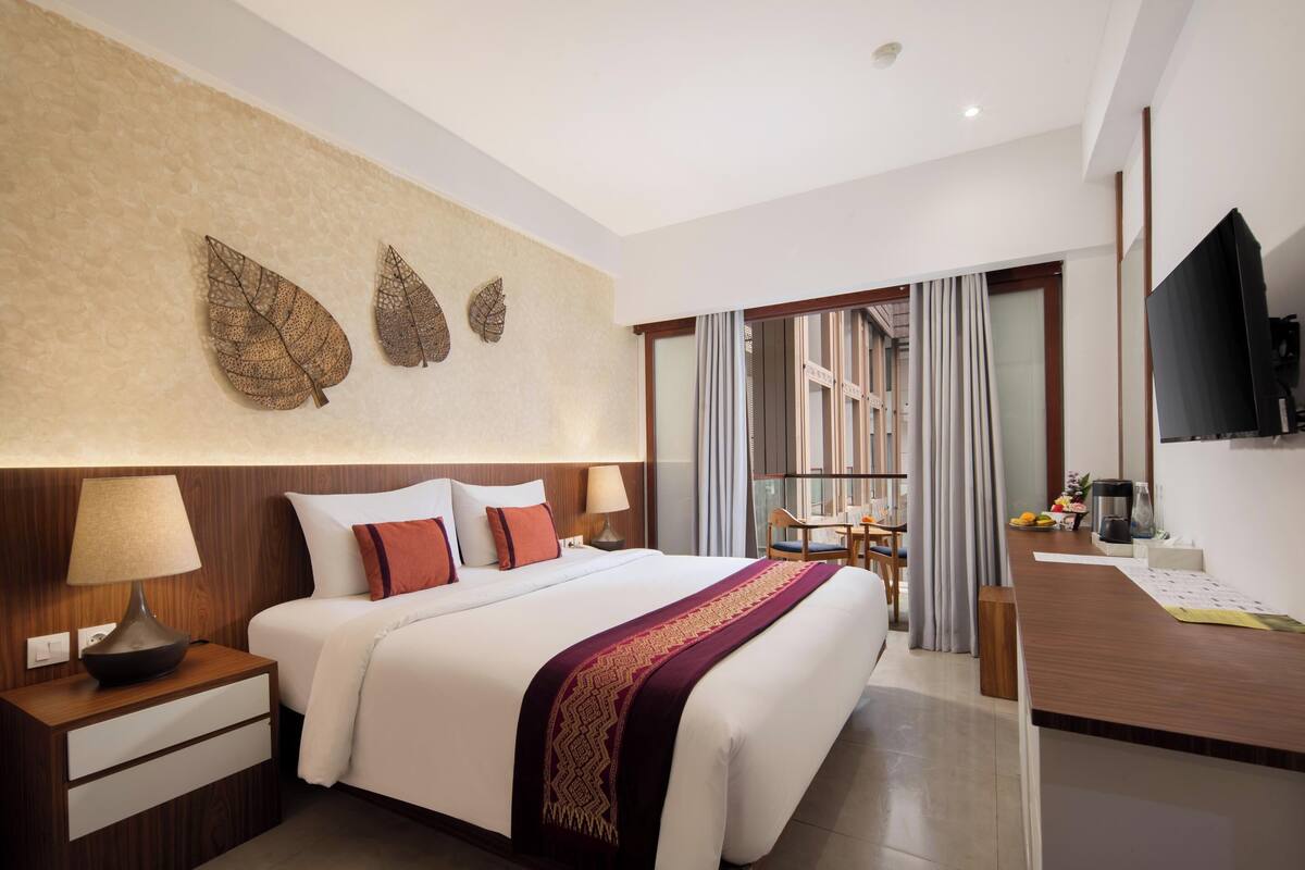A hotel room with a bed, bedside tables, a TV, a desk, and a view of the outside.