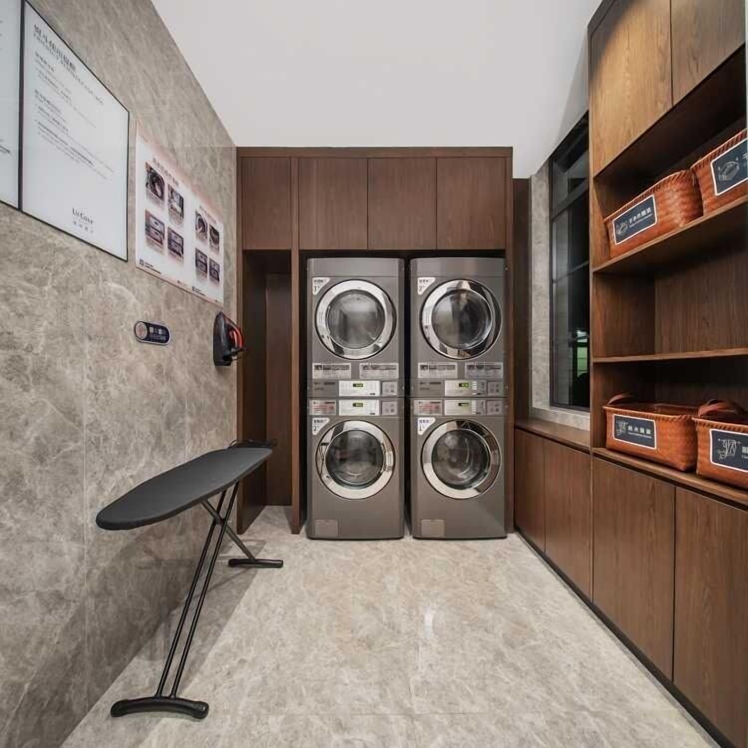 A laundry room with two washing machines, a drying rack, and wooden shelving with baskets.