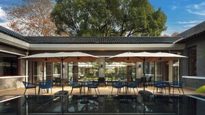 A modern outdoor dining area with glass tables and blue chairs, surrounded by large umbrellas. - UrCove By Hyatt Nanjing Zhongshanling Resort (Nanjing)