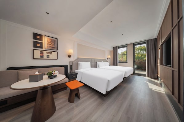 A modern hotel room with a sofa, a small table, a nightstand, a bed, and a TV.