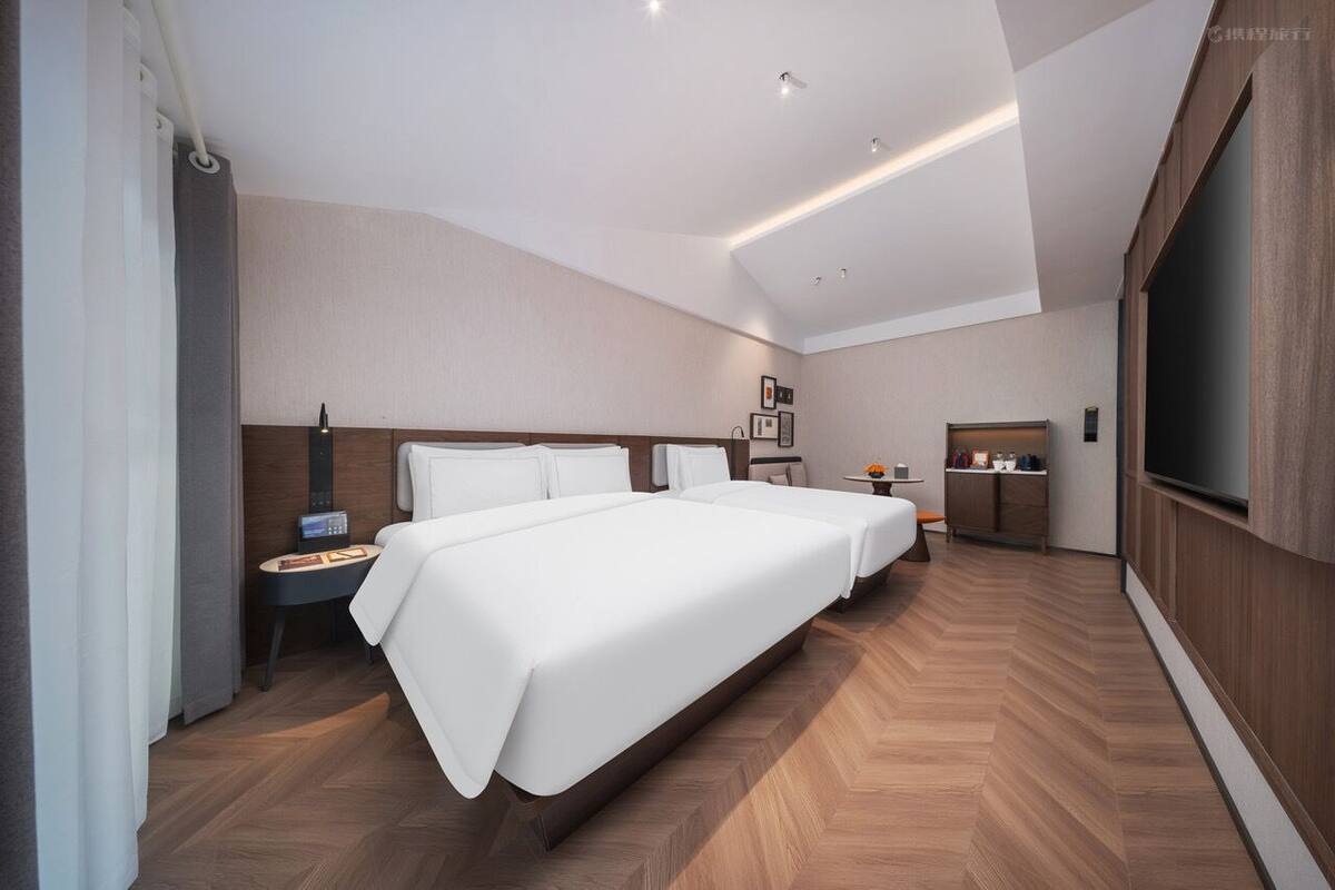 Una habitación de hotel moderna con una cama grande, mesitas de noche, televisión y un escritorio pequeño.