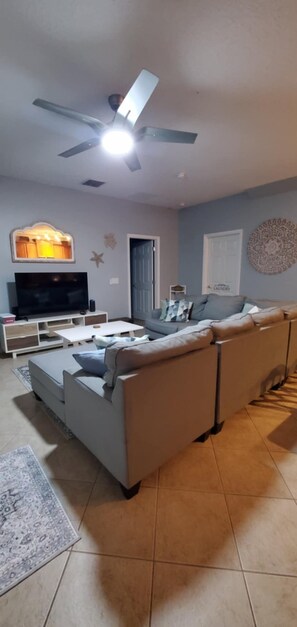 A living room with a sofa, TV, ceiling fan, and decorative wall art.