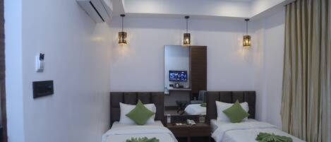 A hotel room with two beds, a ceiling fan, an air conditioner, a TV on a desk, and pendant lights.