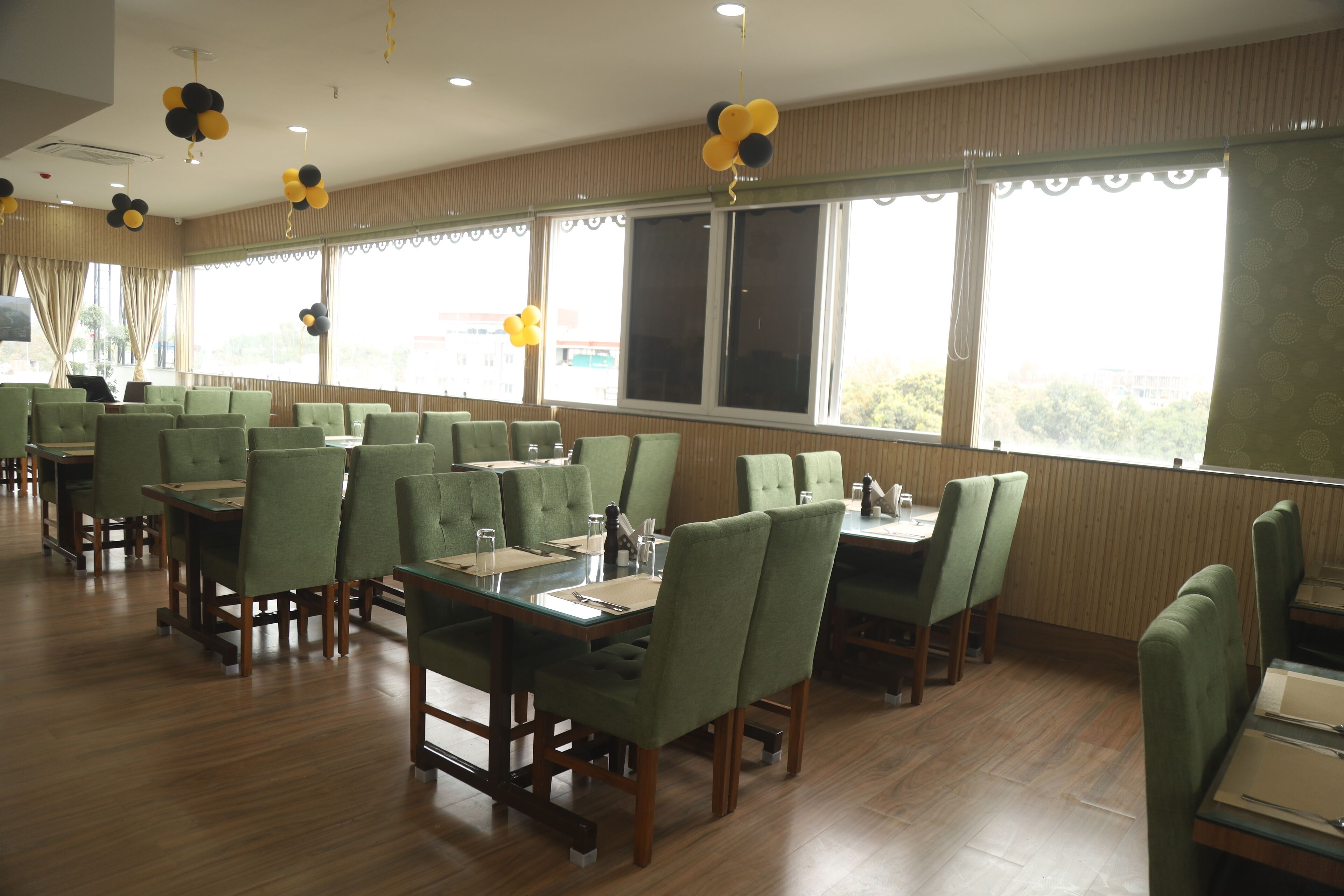 Un comedor con sillas tapizadas en verde y mesas, ventanas amplias y adornos en el techo.