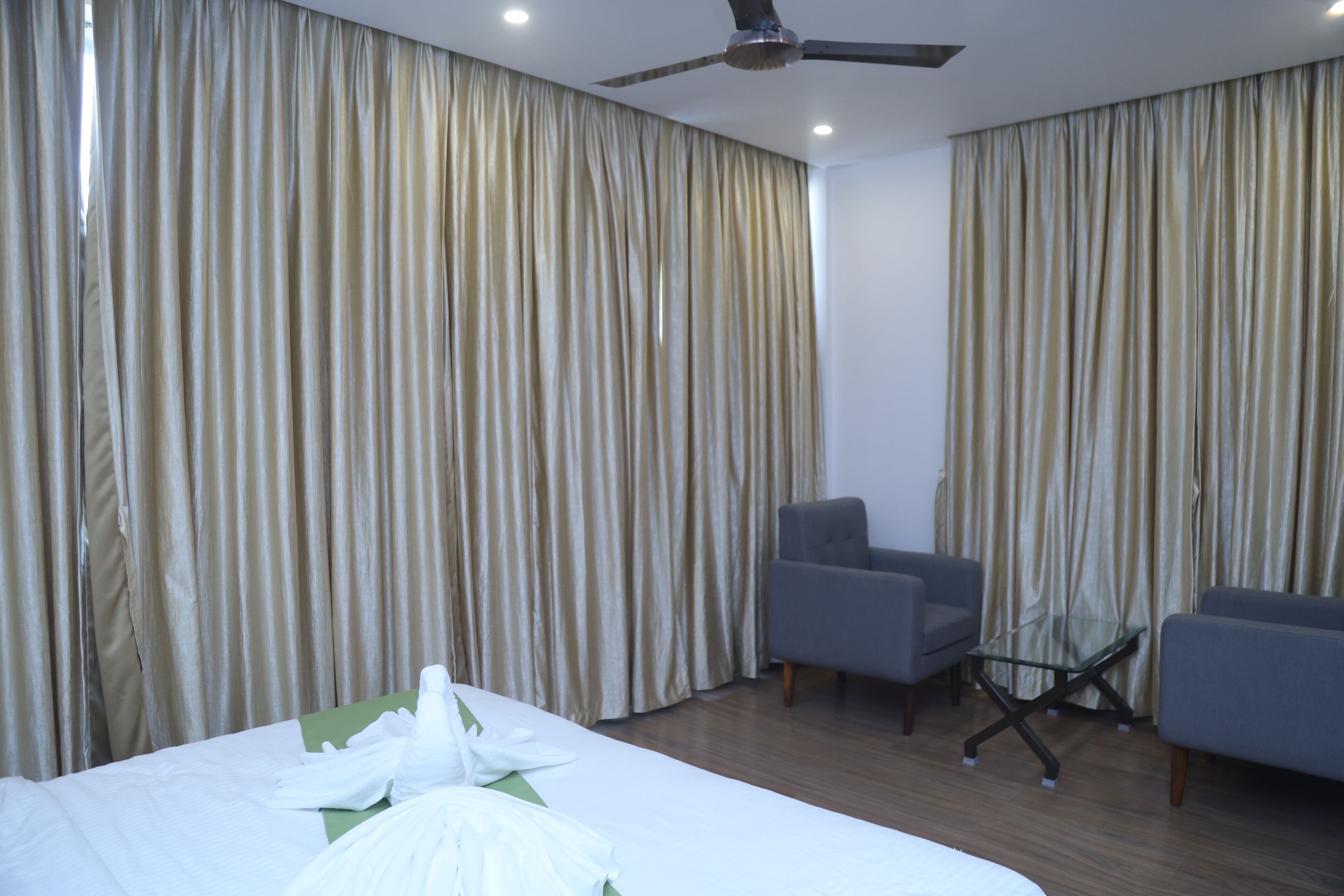 Habitación de hotel con cama, dos sillones, una mesita y un ventilador de techo.