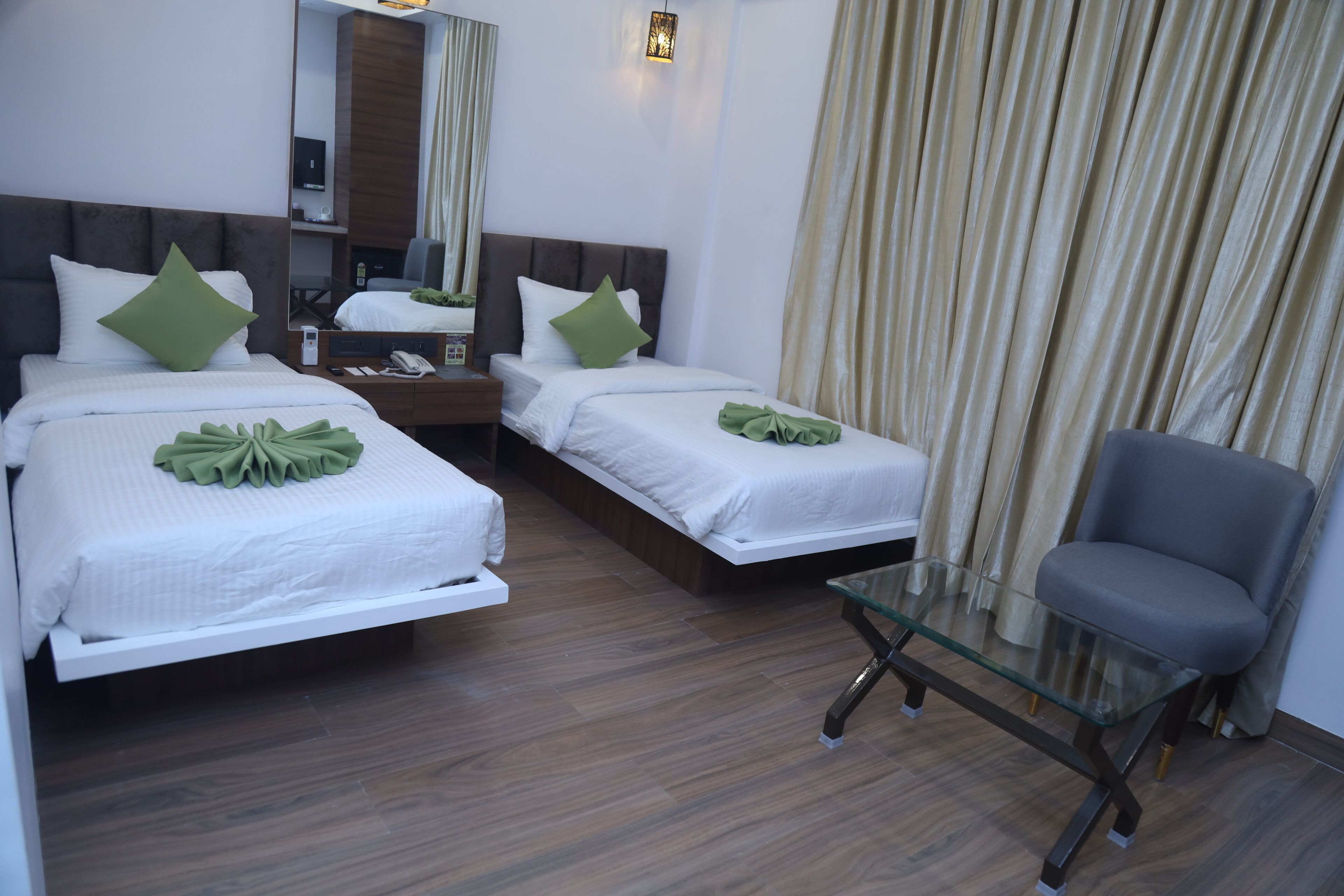 Habitación de hotel con dos camas, una mesita de vidrio, una silla y un espejo.