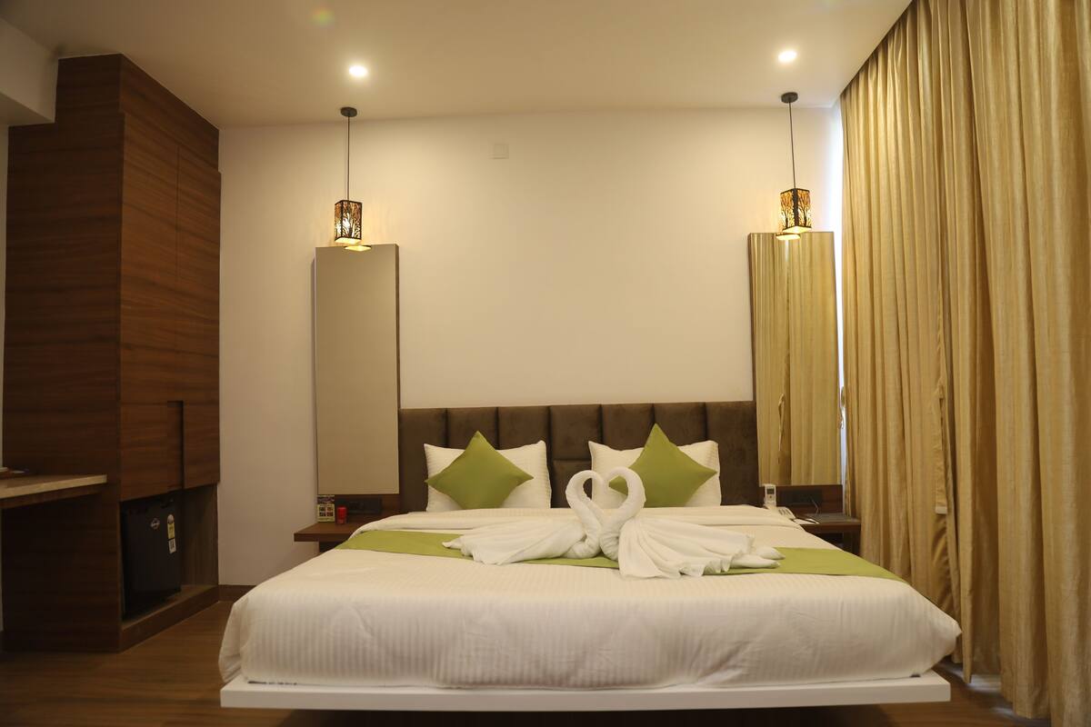 A hotel room with a large bed, a wooden wardrobe, a bedside table, and a mirror.